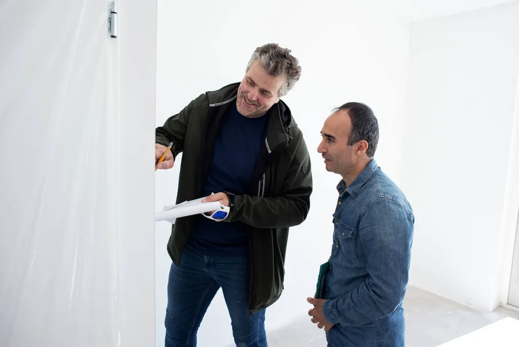 Een medewerker doet samen met een nieuwe bewoner een inspectie van een net opgeleverd, leeg nieuwbouwhuis