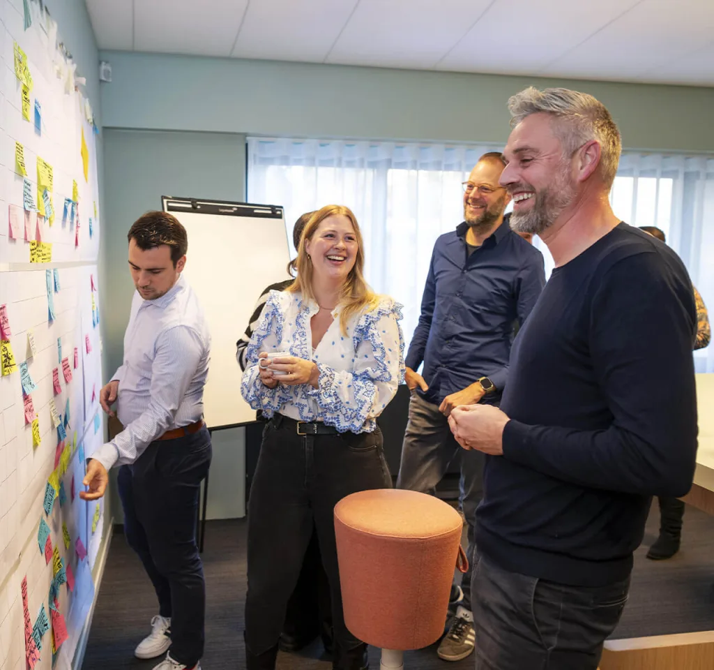 Medewerkers staan op kantoor voor een bord met post-its en hebben een brainstorm over projecten in de woningcorporatiesector
