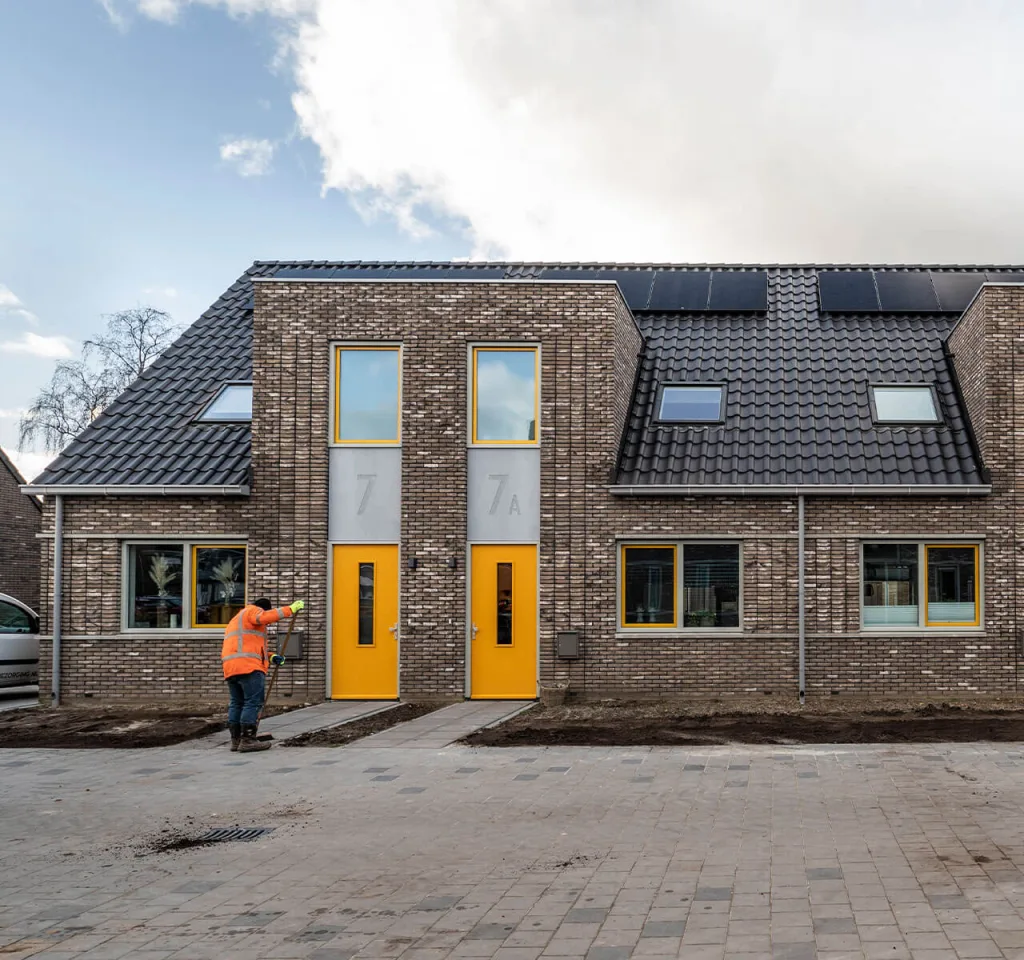 Een medewerker van een woningcorporatie veegt de stoep bij een net opgeleverde rijtjeswoning in een nieuwbouwwijk